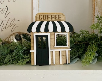May include: A wooden coffee shop sign with a black and white striped awning. The sign says "COFFEE" in brown letters.