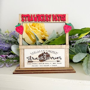 以下が含まれることがあります： 「STRAWBERRY PATCH」と「LOCALLY GROWN strawberries YOU PICK | OPEN DAILY | WE PICK JELLIES - ICE CREAM - SYRUP」と書かれた看板が付いた木製のスタンド。スタンドは赤と緑のイチゴの切り抜きで飾られています。