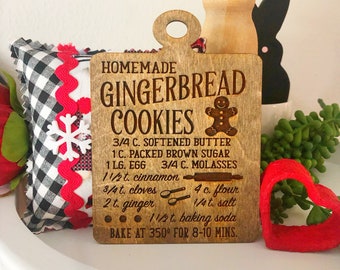 May include: A wooden sign with a gingerbread man graphic and the text "HOMEMADE GINGERBREAD COOKIES" and a recipe for gingerbread cookies. The recipe includes ingredients like softened butter, brown sugar, molasses, cinnamon, cloves, ginger, flour, salt, and baking soda. The sign also includes instructions to bake at 175 degrees Celsius for 8-10 minutes.