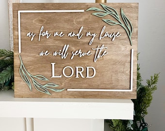 May include: Wooden sign with the quote "as for me and my house we will serve the LORD" in white script. The sign has a brown wood grain background with a white border and green leaf accents. A candle sits on top of the sign.