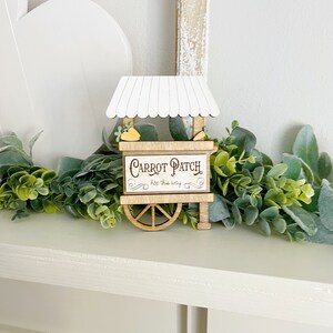 May include: A wooden carrot patch sign with a white awning and a wheel. The sign reads "Carrot Patch hop this way".