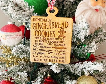 May include: A wooden gingerbread cookie ornament with a gingerbread man illustration and a recipe for homemade gingerbread cookies. The recipe includes ingredients like softened butter, brown sugar, molasses, cinnamon, cloves, ginger, flour, salt, and baking soda. The ornament is decorated with a red and white checkered ribbon.