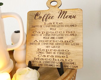May include: A wooden sign with a coffee menu listing different coffee drinks, including latte, cappuccino, americano, espresso, caramel, and macchiato. The sign is brown with a light wood grain and has a handle at the top.
