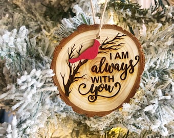 May include: A wooden Christmas bauble featuring a red cardinal perched on a branch. The bauble is engraved with the words "I am always with you".