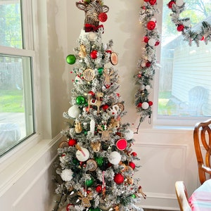 May include: A flocked Christmas tree decorated with red and green baubles, wooden name tags, and various reindeer-themed accents. A large reindeer head topper with a red nose and a plaid bow sits at the peak, while a matching garland hangs nearby.