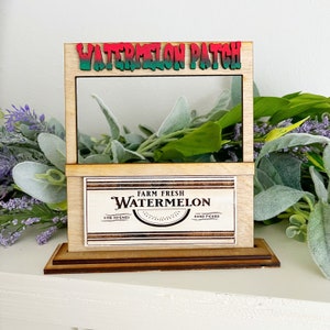 May include: A wooden watermelon patch stand with a sign that reads "Watermelon Patch". The stand has a shelf with a sign that reads "Farm Fresh Watermelon Vine Ripened Hand Picked".