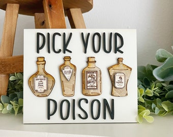May include: White wooden sign with black text that reads "Pick Your Poison". Four wooden bottles with labels are attached to the sign. The labels read "High Quality Small Slime", "Elixir of Life", "Dragon's Breath", and "The Unforgiven".
