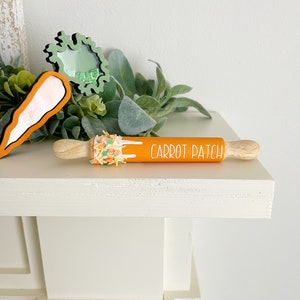 Pode incluir: Rolo de massa laranja e branco com o texto "Carrot Patch" nele. O rolo é decorado com confeitos laranja e verdes.