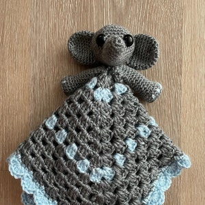 May include: A gray crocheted elephant baby blanket with blue accents. The elephant is attached to the blanket and has black eyes.