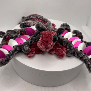 May include: A crocheted dragon with pink and gray fur, silver and pink scales, and black eyes.