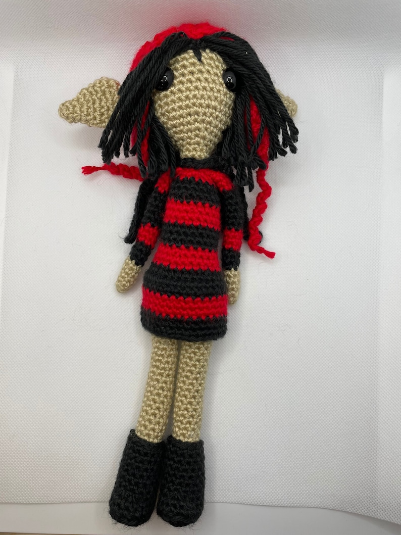May include: A crocheted elf doll with black hair, a red and black striped dress, and black shoes.