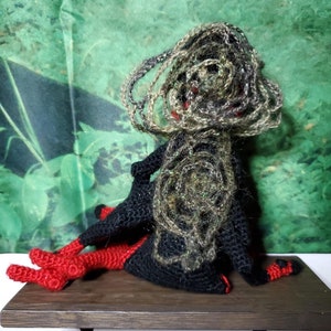 May include: A crocheted doll with black and green yarn for the body and hair, and red yarn for the legs. The doll is sitting on a wooden shelf.