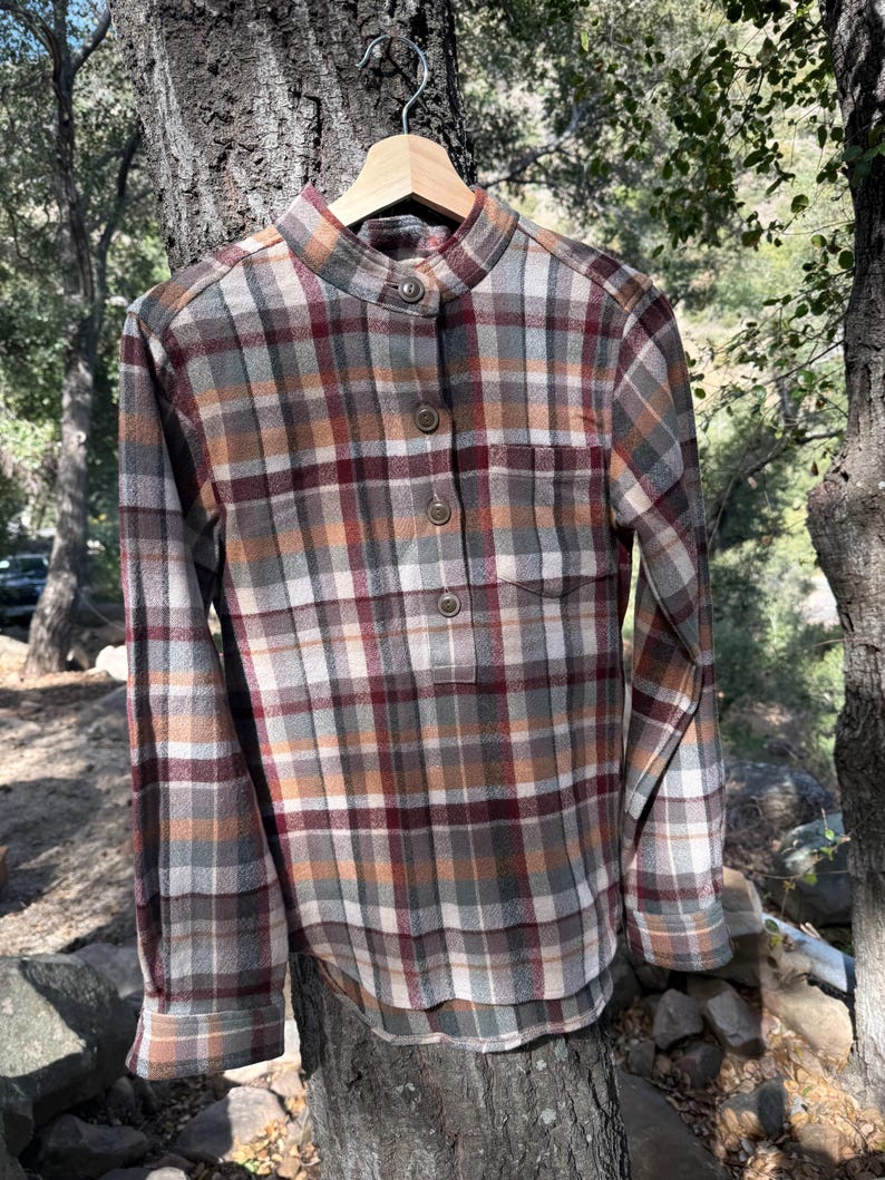 Pode incluir: Uma camisa de manga comprida xadrez com colarinho mandarim e fecho de bot&otilde;es. A camisa &eacute; xadrez marrom, bege e vermelho.