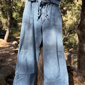 K&ouml;nnte beinhalten: Eine hellblaue Jeanshose mit weitem Bein, hoher Taille und einem breiten G&uuml;rtel, der vorne gebunden wird.
