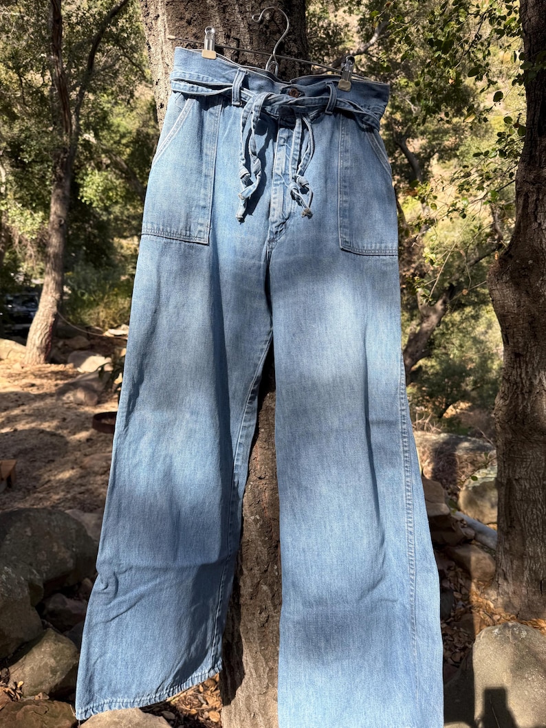 K&ouml;nnte beinhalten: Eine hellblaue Jeanshose mit weitem Bein, hoher Taille und einem breiten G&uuml;rtel, der vorne gebunden wird.