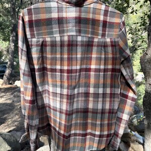 Pode incluir: Uma camisa de manga comprida xadrez com um padr&atilde;o xadrez marrom, bege, verde e vermelho. A camisa tem um colarinho abotoado e um caimento relaxado.