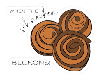 Pode incluir: Um autocolante com três rolos de canela castanhos em forma de espiral com espirais de glacê castanho escuro. O texto "WHEN THE" está impresso a preto, seguido da palavra cursiva "schnecken" e "BECKONS!" em letras maiúsculas.