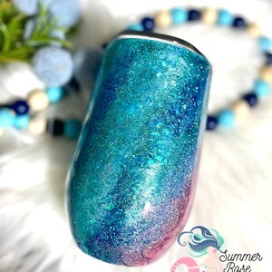 May include: A glitter-covered tumbler in shades of teal, turquoise, and pink. The stainless steel wine tumbler has a black rim and a rounded base. The Summer Rose Shoppe logo is visible in the lower right corner.