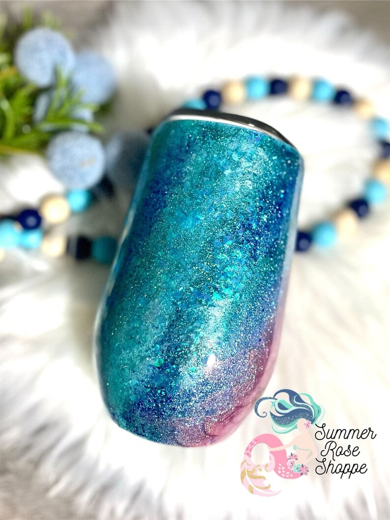 May include: A glitter-covered tumbler in shades of teal, turquoise, and pink. The stainless steel wine tumbler has a black rim and a rounded base. The Summer Rose Shoppe logo is visible in the lower right corner.