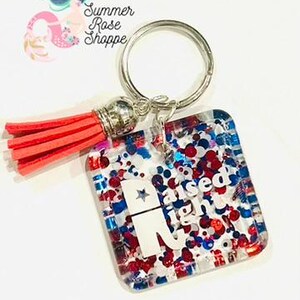May include: A square keychain with a silver ring and a red tassel. The keychain has a clear background filled with red, white, and blue glitter and the text "Raised Right" with a star. The keychain is from Summer Rose Shoppe.