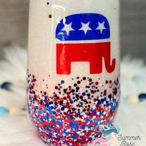 May include: A stemless wine tumbler with a glittery white finish. The tumbler features a red, white, and blue Republican Party elephant logo. The bottom of the tumbler is covered in red, white, and blue glitter.