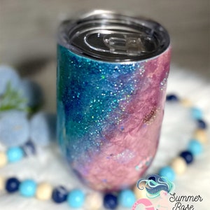 May include: A glitter-covered tumbler with a lid, featuring a gradient of blue and pink hues. The design includes sparkling glitter accents, creating a shimmering effect. The tumbler is designed to keep beverages cold or hot. The Summer Rose Shoppe logo is visible.