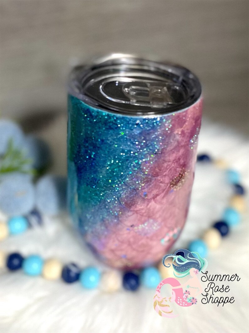 May include: A glitter-covered tumbler with a lid, featuring a gradient of blue and pink hues. The design includes sparkling glitter accents, creating a shimmering effect. The tumbler is designed to keep beverages cold or hot. The Summer Rose Shoppe logo is visible.