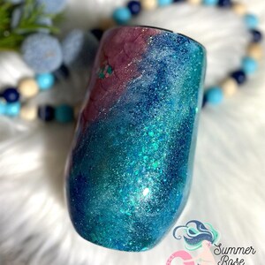 May include: A stemless wine tumbler with a glittery, ocean-themed design. The tumbler features a gradient of colors, including teal, blue, and purple, with sparkling glitter accents. The Summer Rose Shoppe logo is visible in the bottom right corner.