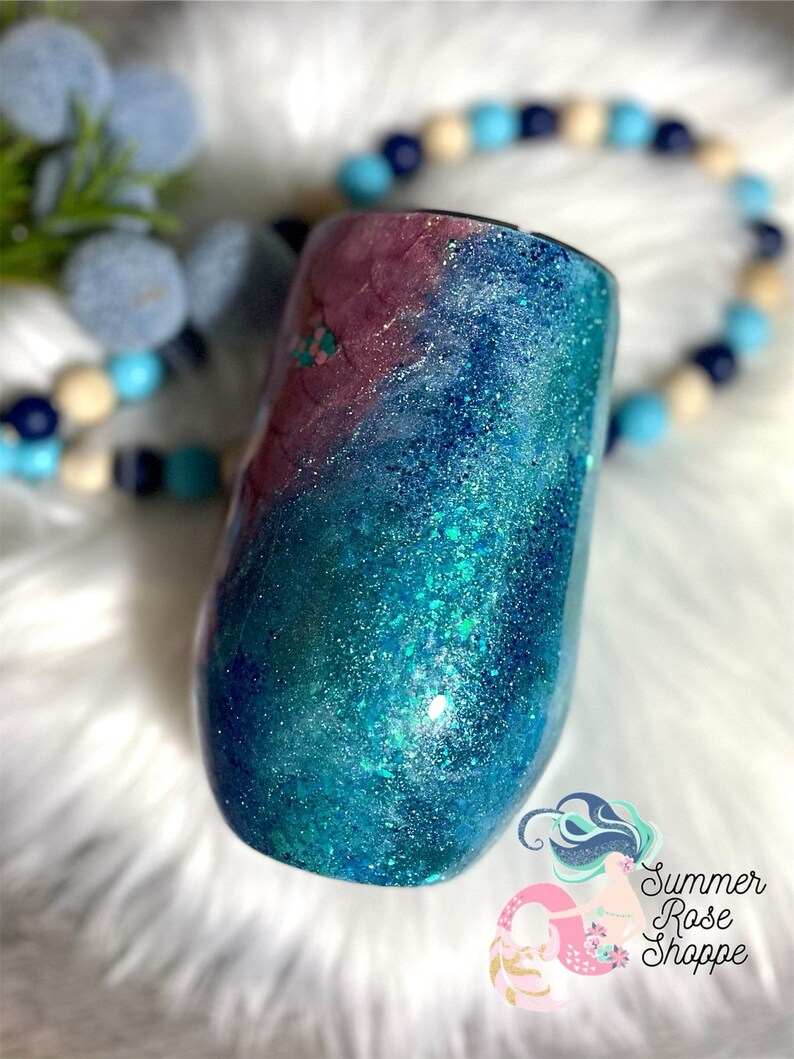 May include: A stemless wine tumbler with a glittery, ocean-themed design. The tumbler features a gradient of colors, including teal, blue, and purple, with sparkling glitter accents. The Summer Rose Shoppe logo is visible in the bottom right corner.