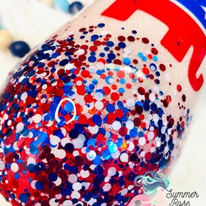 May include: A glitter-covered tumbler with red, white, and blue confetti. The design includes a red elephant graphic with a blue star-studded top. The tumbler is a patriotic theme.