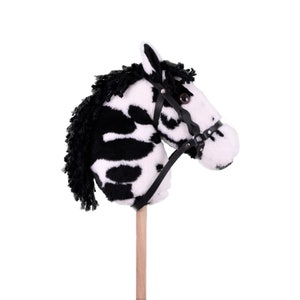 May include: A black and white zebra-patterned plush horse head on a wooden stick. The horse has a black leather bridle with a buckle.