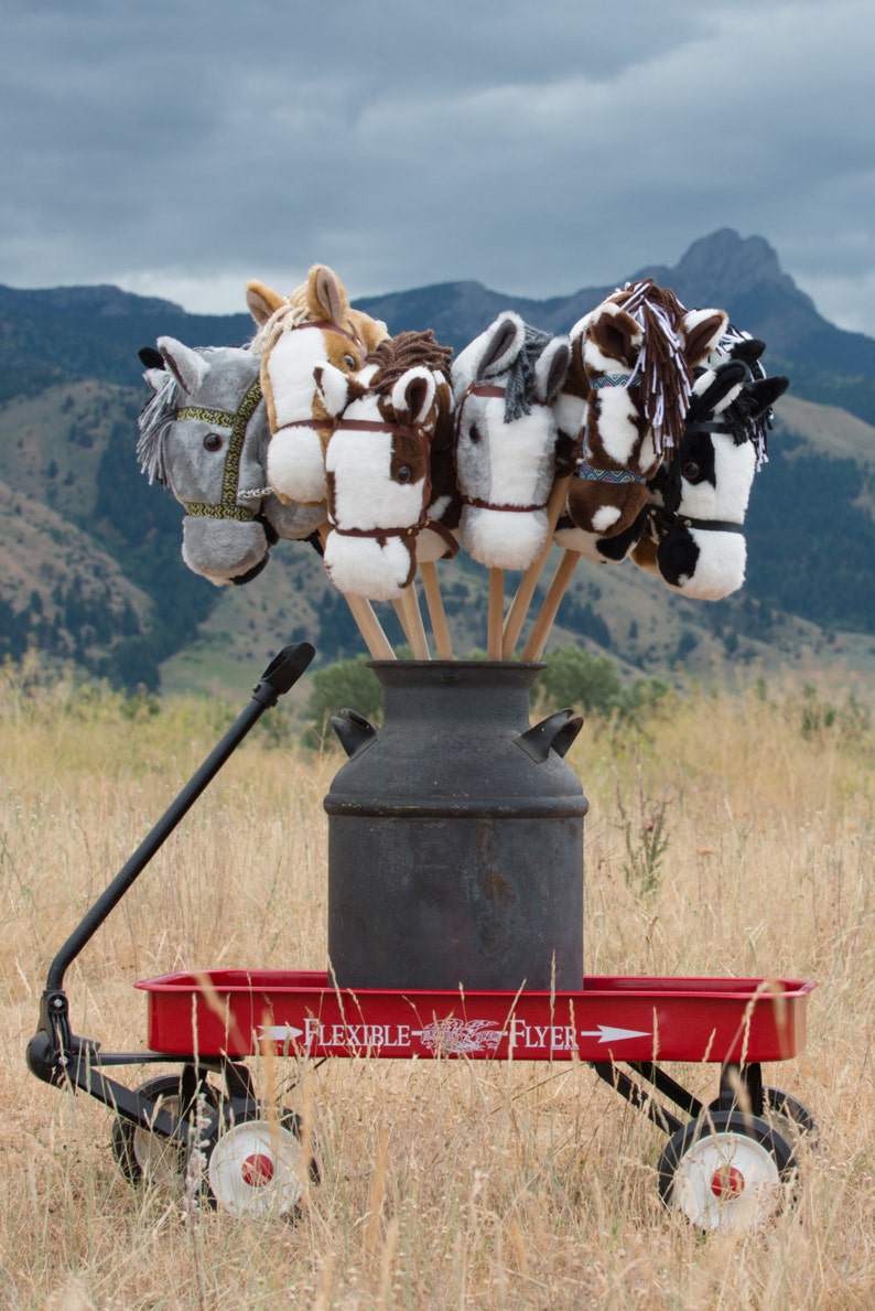 May include: A red wagon with a black milk can and six plush horse head toys on wooden sticks. The wagon has the words "Flexible Flyer" printed on the side.