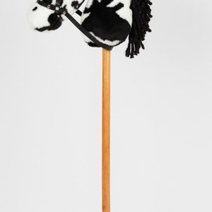 May include: A black and white spotted plush horse head on a wooden stick. The horse has a black mane and a black leather bridle.