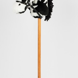 May include: A black and white plush horse head on a wooden stick. The horse has a black leather bridle.