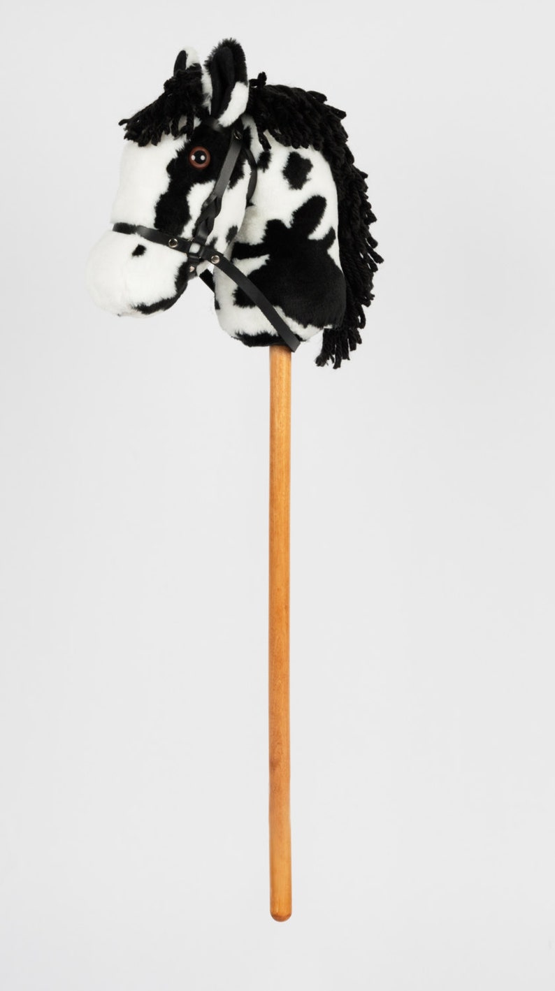 May include: A black and white plush horse head on a wooden stick. The horse has a black leather bridle.