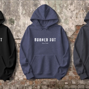 May include: Three hooded sweatshirts in black, blue, and gray with the text "Burned Out" in white lettering on the front. The text is centered and includes the words "New York" underneath.