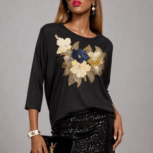 May include: A black three-quarter sleeve top featuring a central floral appliqué made of gold, beige, and navy blue sequins. The top is paired with a black sequined mini skirt, a black sequined headband, oversized square sunglasses, and a black clutch.