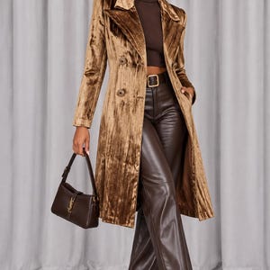 May include: A long-sleeved, double-breasted bronze velvet coat with a notched collar and decorative buttons, paired with a dark brown ribbed turtleneck, dark brown leather trousers with a belt, dark brown pointed-toe boots, and a dark brown handbag.