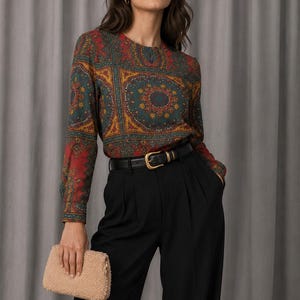May include: A long-sleeved blouse featuring a multi-colored intricate mandala-style pattern in shades of red, teal, and gold, paired with high-waisted black trousers, a black leather belt with a gold buckle, and a beige textured fuzzy clutch bag.