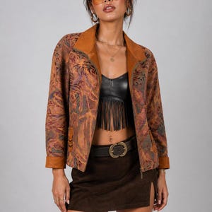 May include: A brown patterned jacket with a tan collar and cuffs. The jacket is paired with a black top, brown skirt, and a belt with a gold buckle. The model is wearing sunglasses and gold jewelry.