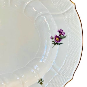 May include: White porcelain serving platter with a scalloped edge and a gold rim. The platter features a delicate floral design with purple flowers and green leaves.