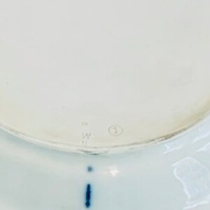 May include: The underside of a white ceramic plate with a blue mark and the number "1" in a circle.