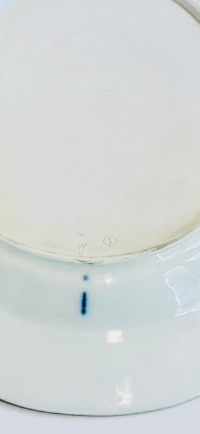 May include: The underside of a white ceramic plate with a blue mark and the number "1" in a circle.