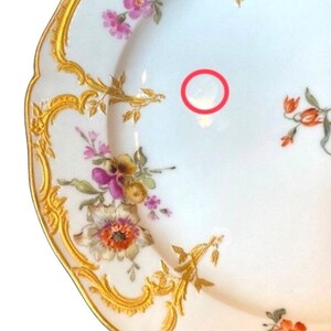 May include: A white porcelain plate with a gold rim and floral pattern. The plate has a scalloped edge and is decorated with pink, yellow, and orange flowers.