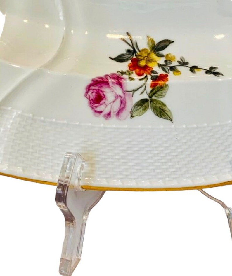 May include: White porcelain serving dish with a floral design featuring pink, red, yellow, and green flowers. The dish has a woven pattern around the edge and a gold trim.