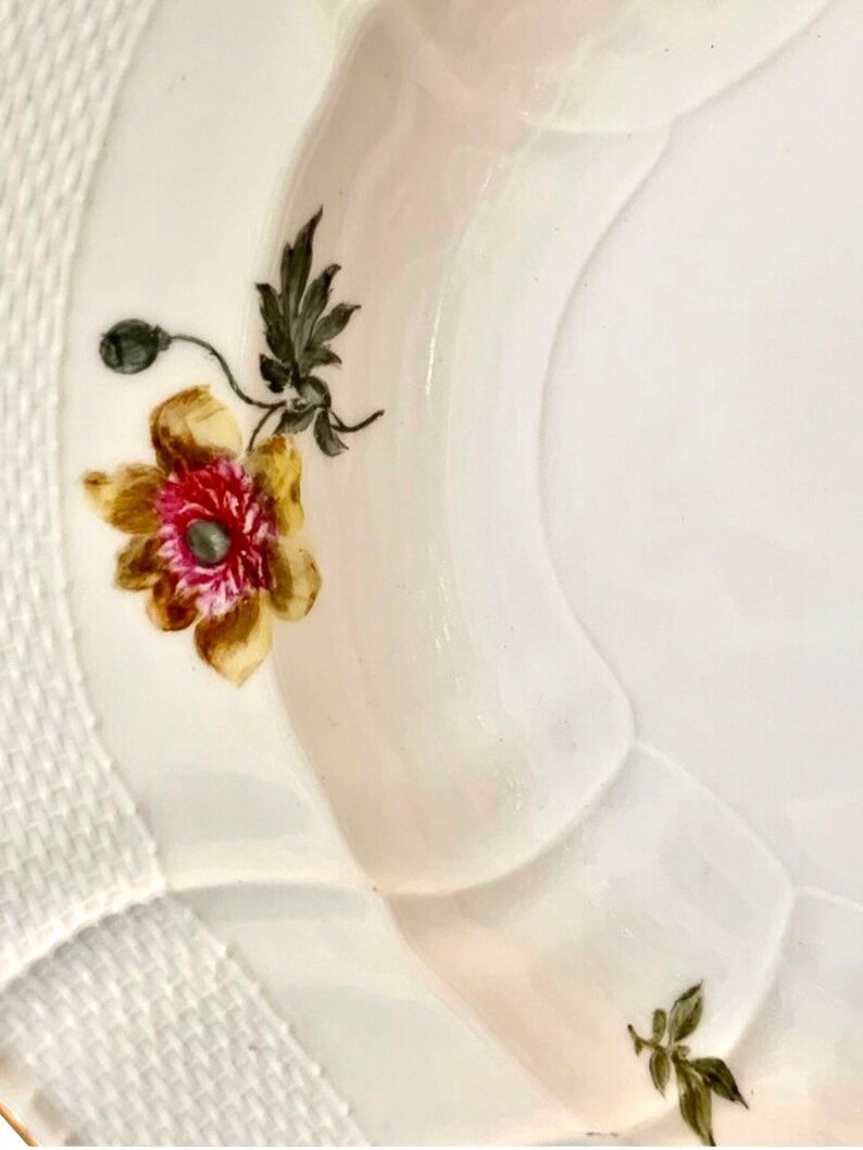 May include: A white porcelain bowl with a scalloped edge and a floral design. The bowl features a yellow and brown poppy with a pink center and green leaves. The bowl has a white woven pattern around the rim.