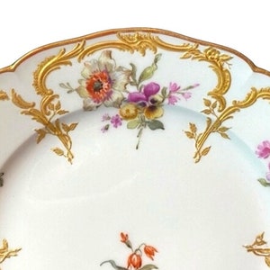 May include: A white porcelain plate with a gold rim and floral pattern. The plate features a delicate floral design with pink, purple, and orange flowers. The gold rim is intricate and adds a touch of elegance to the plate.