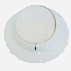 May include: The underside of a white porcelain plate with a scalloped edge. The plate has a blue mark on the bottom.