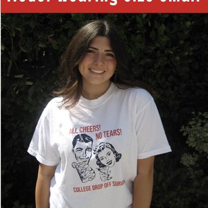 May include: A white t-shirt with a black and white illustration of a man and woman holding drinks. The text on the shirt reads "All Cheers! No Tears! College Drop Off Survived".