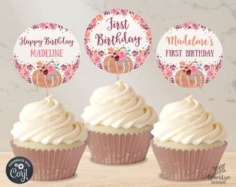 May include: Three cupcakes with white frosting and pink cupcake liners. Each cupcake has a round topper with floral designs and the text "Happy Birthday Madeline", "First Birthday", and "Madeline's First Birthday".